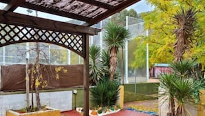 A covered outdoor area with a wooden pergola, potted plants, and a red tiled floor.