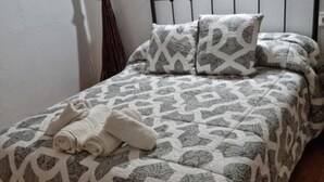 Un lit avec une couvre-lit à motifs et deux oreillers, une serviette enroulée posée sur le lit, et une tête de lit en métal noir.