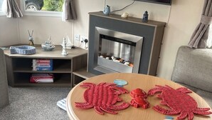 Ein gemütlicher Wohnraum mit Kamin, einem runden Holztisch mit Krabben-Dekorationen und einem Bücherregal mit Kinderspielzeug.