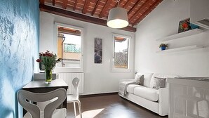 En modern inredning med en vit soffa, ett matbord med stolar, en hänglampa och en utsikt genom ett fönster.