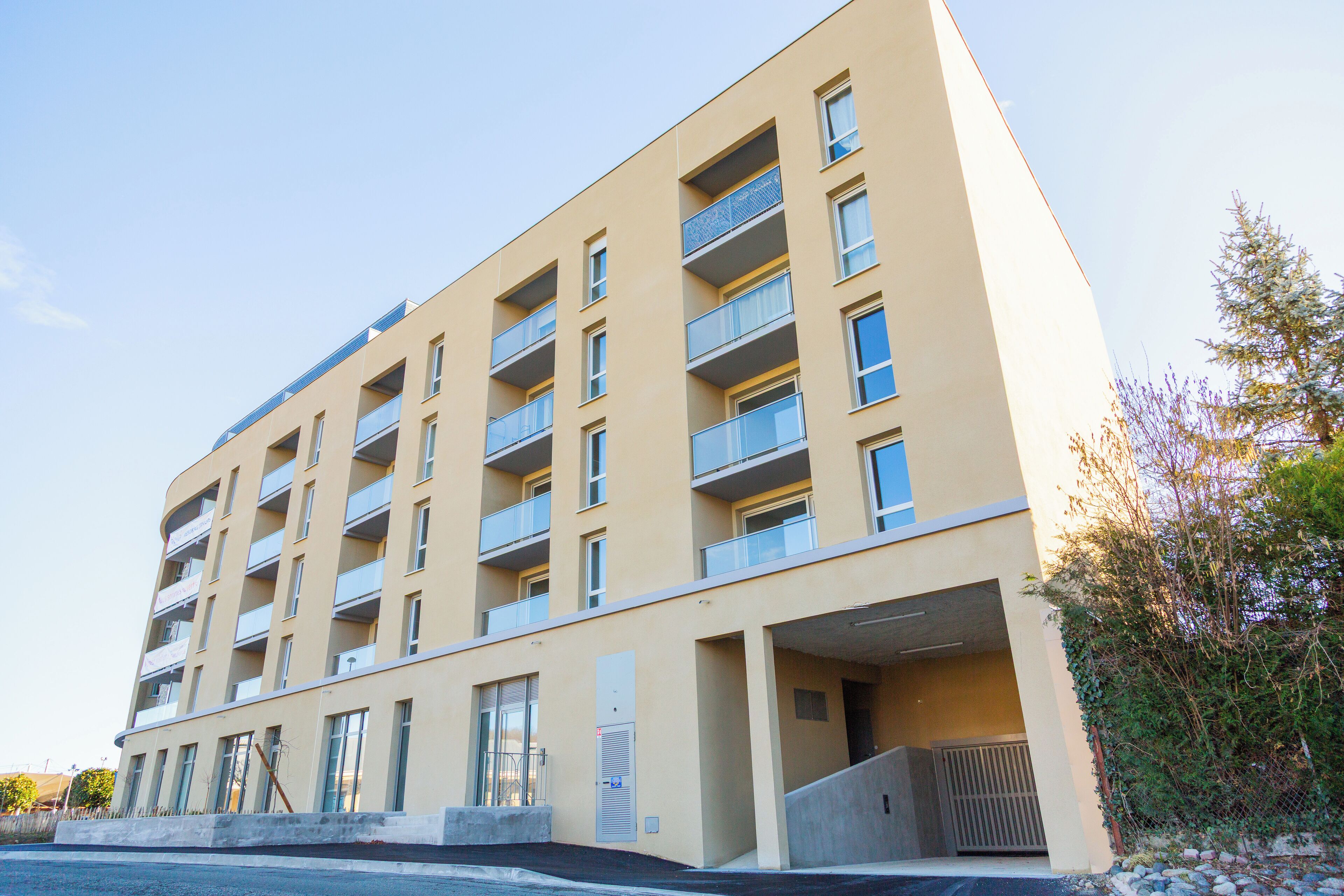 Un immeuble à plusieurs étages, doté de balcons, d’une façade plane et d’un espace de stationnement.