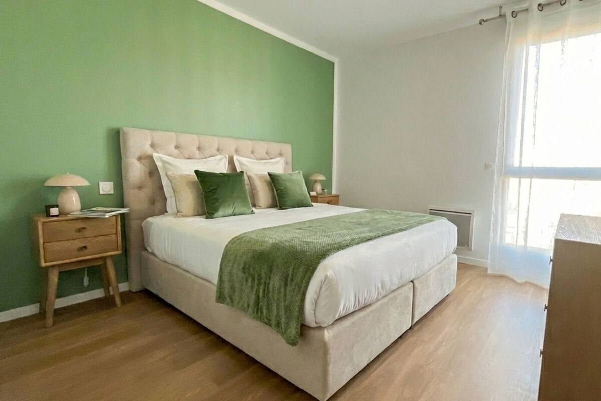A bedroom with a bed, bedside tables, a nightstand, a window with curtains, and a green wall.