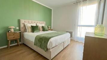 Een slaapkamer met een bed, nachtkastjes, een raam met gordijnen en een groene wand.