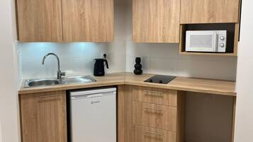 Una cocina compacta con armarios de madera, microondas integrado, un lavamanos y lavavajillas.