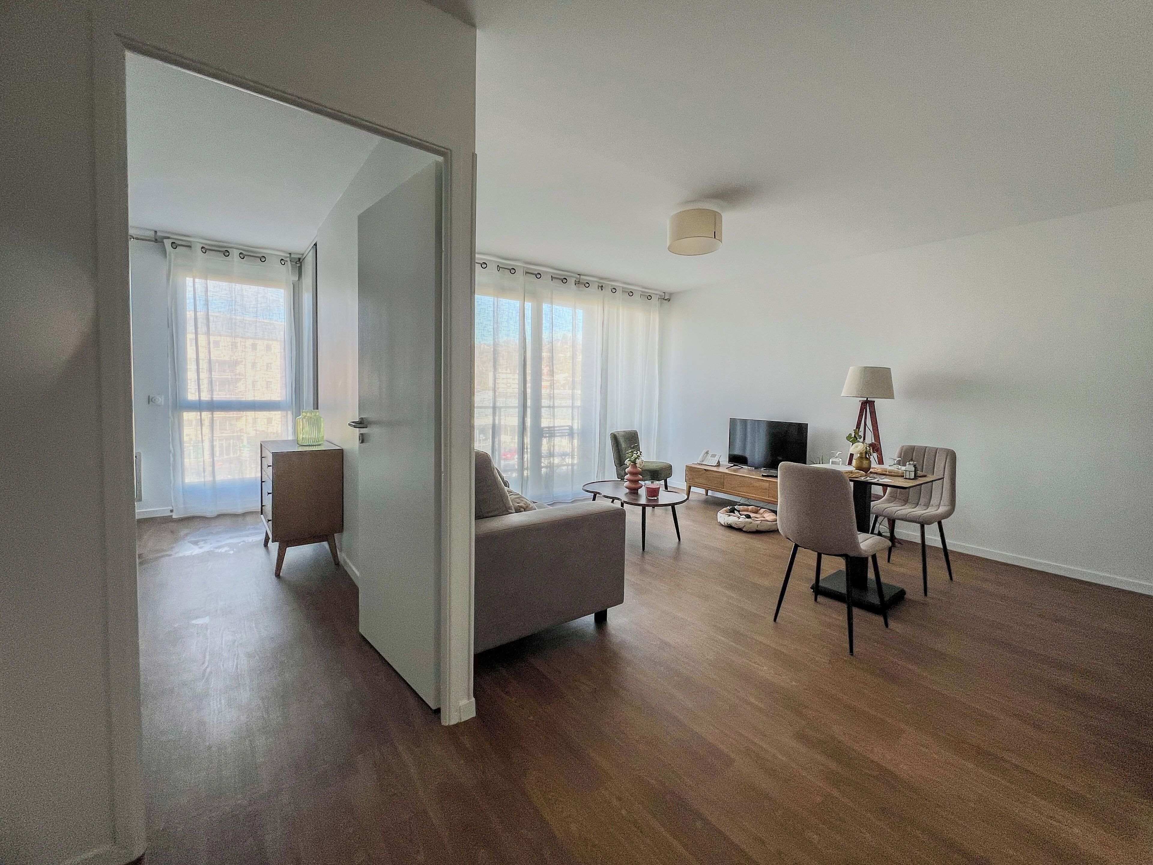 Una sala de estar moderna con un sofá, una mesa de centro, un televisor y una lámpara. Hay una puerta que conduce a otra habitación.