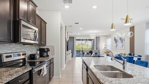 A modern kitchen with dark cabinetry, stainless steel appliances, and a granite countertop. - Stylish 6BR Home with Themed Rooms and Pool (Davenport)