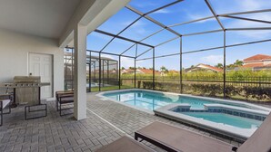 A covered outdoor swimming pool with lounge chairs, a barbecue grill, and a view of the neighborhood. - Stylish 6BR Home with Themed Rooms and Pool (Davenport)