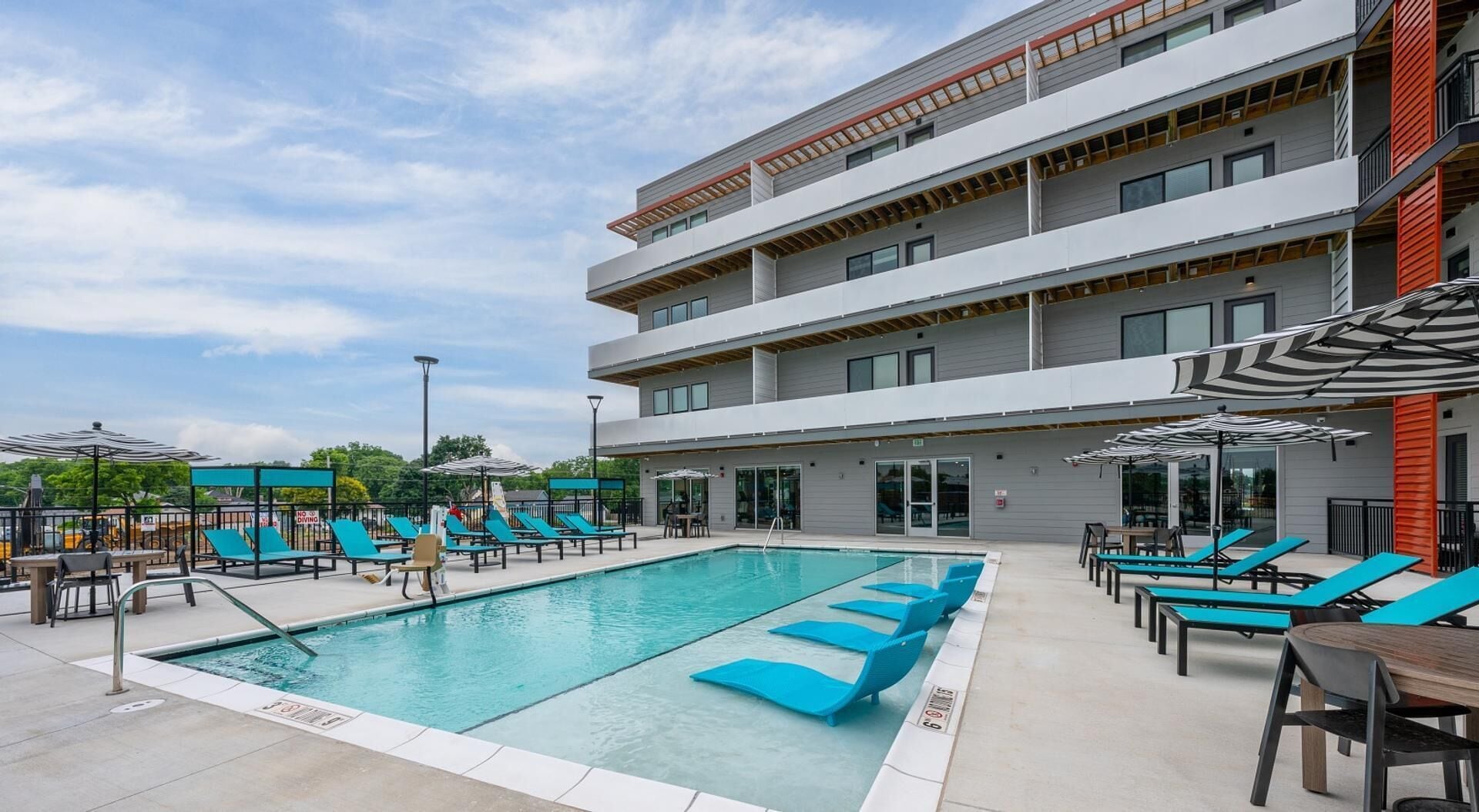 A modern building with a swimming pool, outdoor seating, and a covered area with umbrellas.