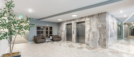Eine moderne Lobby mit einem Marmor-Empfangsbereich, zwei Sitzbereichen und einem Aufzug.