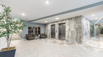 A modern lobby with a marble reception desk, two seating areas, and an elevator.
