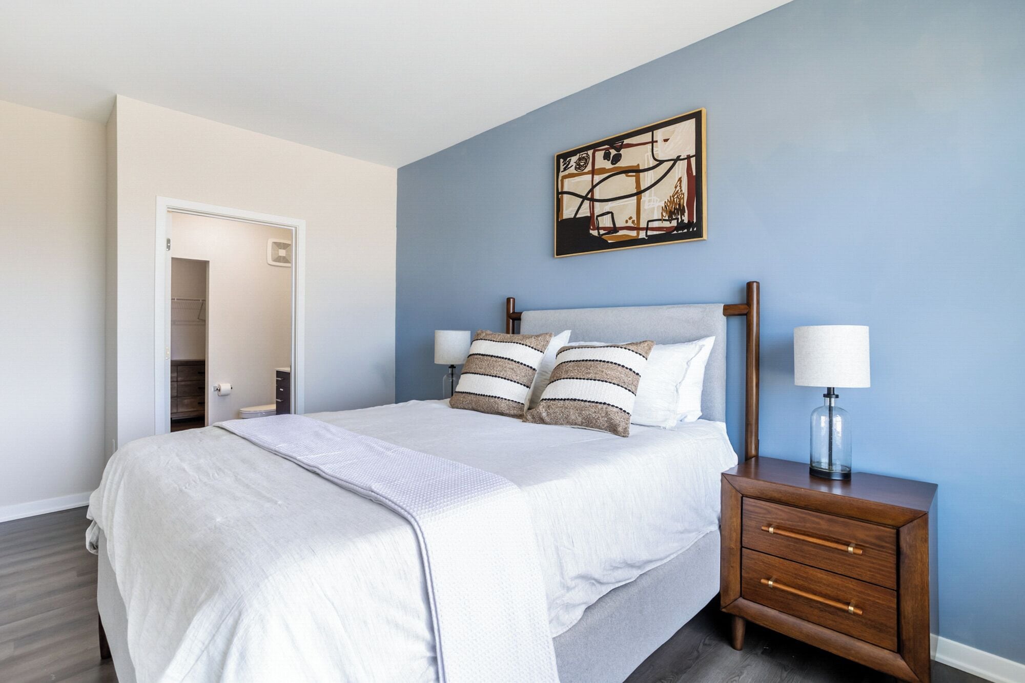 A bedroom with a bed, bedside tables, a wardrobe, and a painting on the wall.