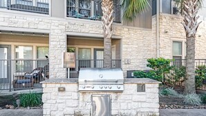 A stone-built outdoor grill area with a patio chair and table, surrounded by a stone wall and a small garden. - Landing Amazing 1bd, Clubhouse, Gym (Houston)