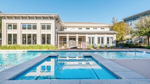 A swimming pool area with a building featuring large windows and a covered patio. - Landing Amazing 1bd, Clubhouse, Gym (Houston)