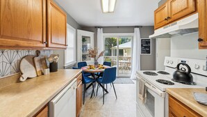 Een keuken met houten kastjes, een witte oven en een eettafel met stoelen.