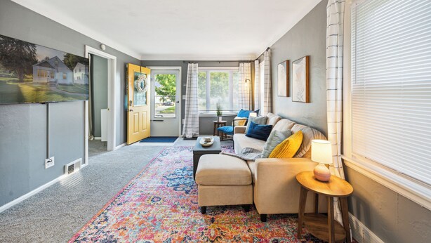 Een gezellige woonkamer met een hoekbank, een klein tafeltje en een kleurrijk vloerkleed.