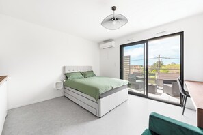 A modern bedroom with a bed, a desk, and a view of the outdoors through a large sliding glass door. - Studio Eucalyptus - Centre - Albi (Albi)