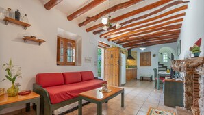 Ein Wohnzimmer mit rotem Sofa, Holzbalken, Fliesenboden und einer Küche im Hintergrund.