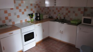 Een keuken met witte kastjes, een fornuis, een magnetron en een spoelbak.