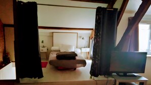 Een slaapkamer met een bed, nachtkastje, televisie en raam.