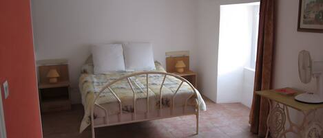 A bedroom with a bed, bedside tables, a desk with a chair, a window with curtains, and a wall-mounted fan.