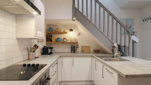 A modern kitchen with white cabinets, a black stove, and a wooden staircase. - The Kiln (Bedford)
