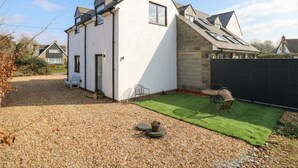 A modern house with a sloped roof, a small patio with a table and chairs, and a gravel driveway. - The Kiln (Bedford)