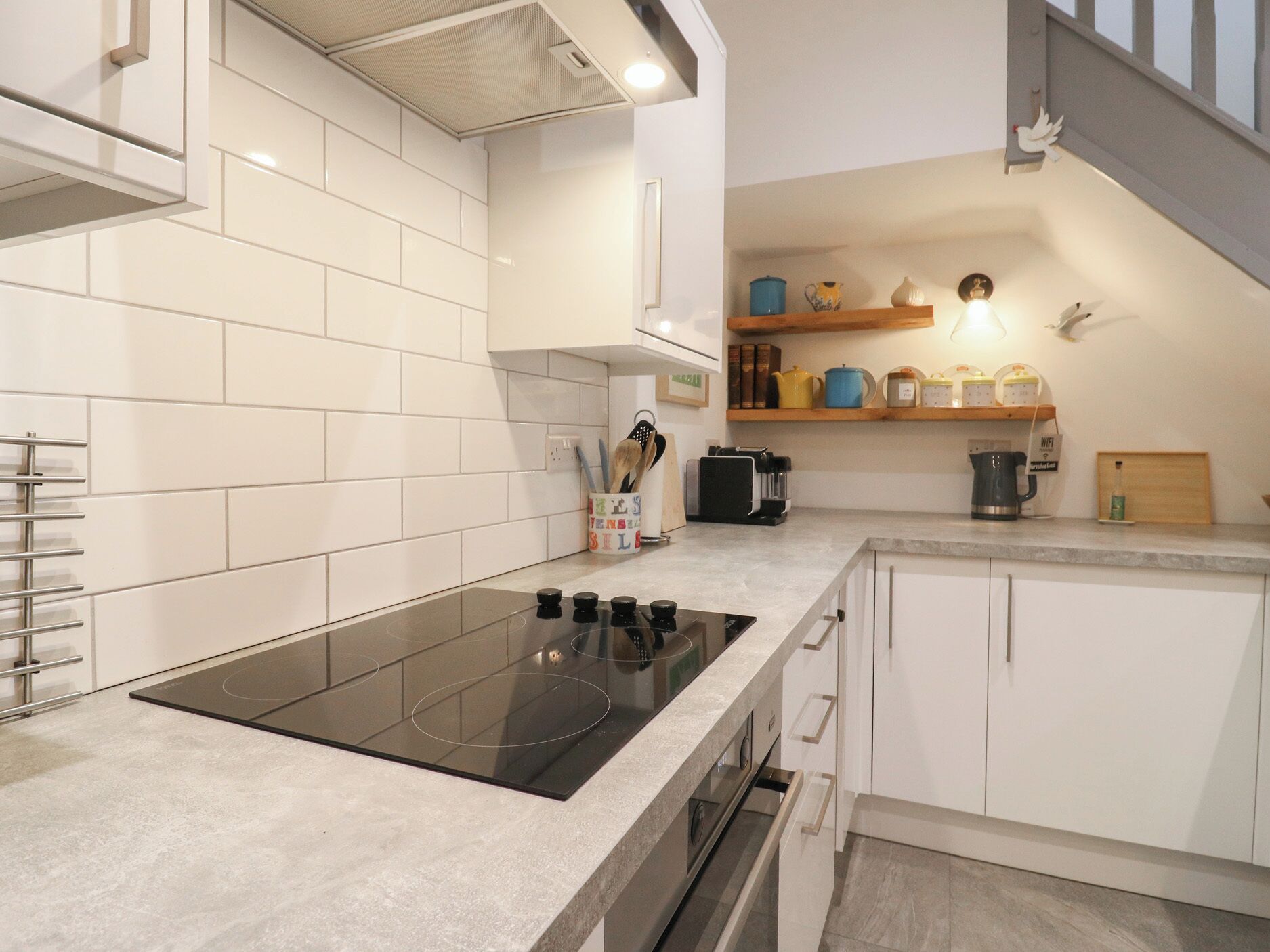 Een moderne keuken met witte kasten, een zwart inductiekookveld en een roestvrijstalen afzuigkap.
