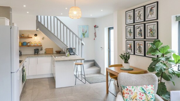 A modern kitchen with a central island, a dining area with a wooden table, and a staircase leading to an upper level. - The Kiln (Bedford)