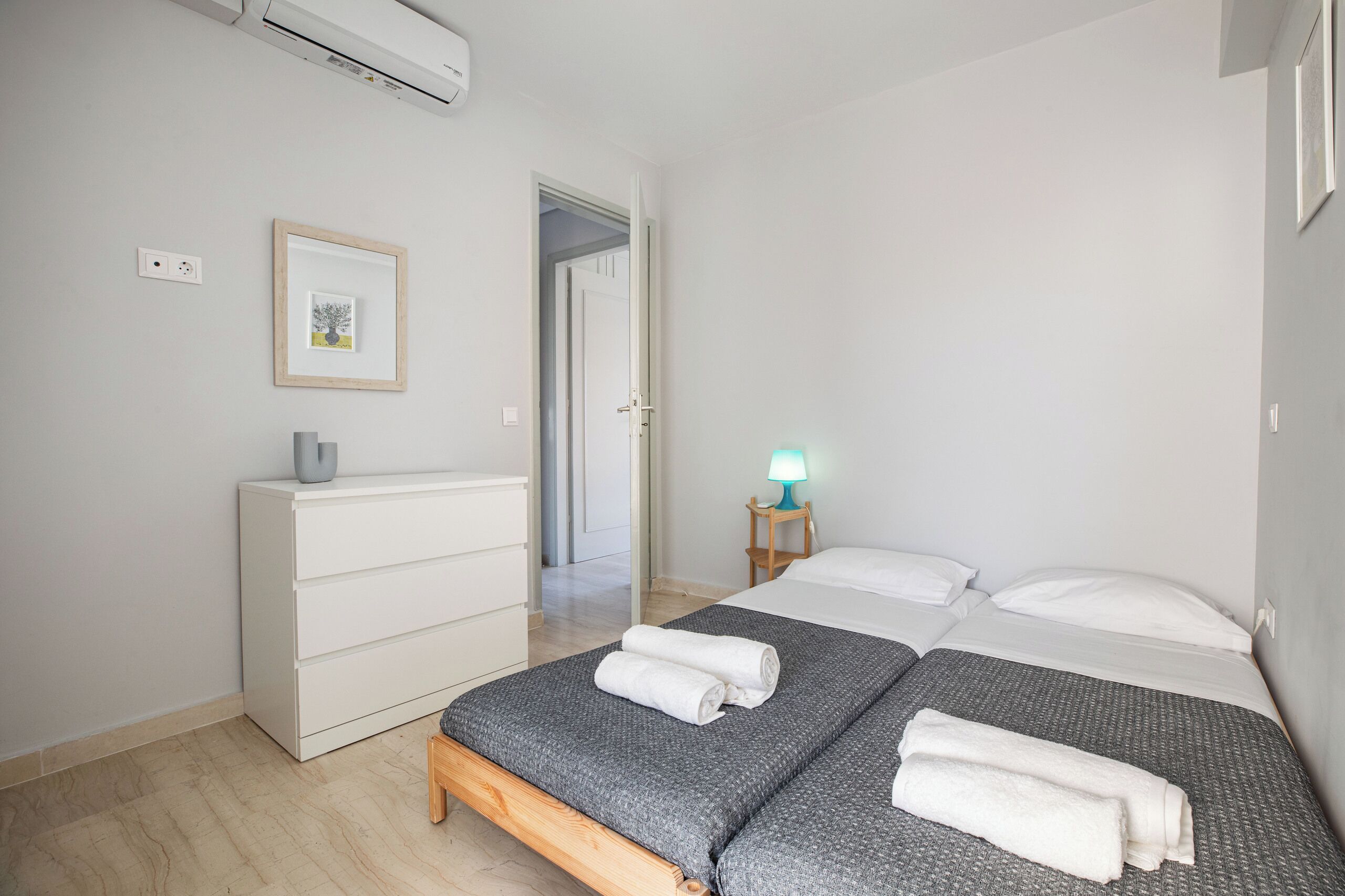 Ein Schlafzimmer mit Bett, Schminktisch, Nachttisch mit Lampe, einem gerahmten Bild an der Wand und einer Tür zu einem weiteren Raum.