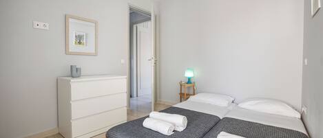 Ein Schlafzimmer mit Bett, Schminktisch, Nachttisch mit Lampe, einem gerahmten Bild an der Wand und einer Tür zu einem weiteren Raum.