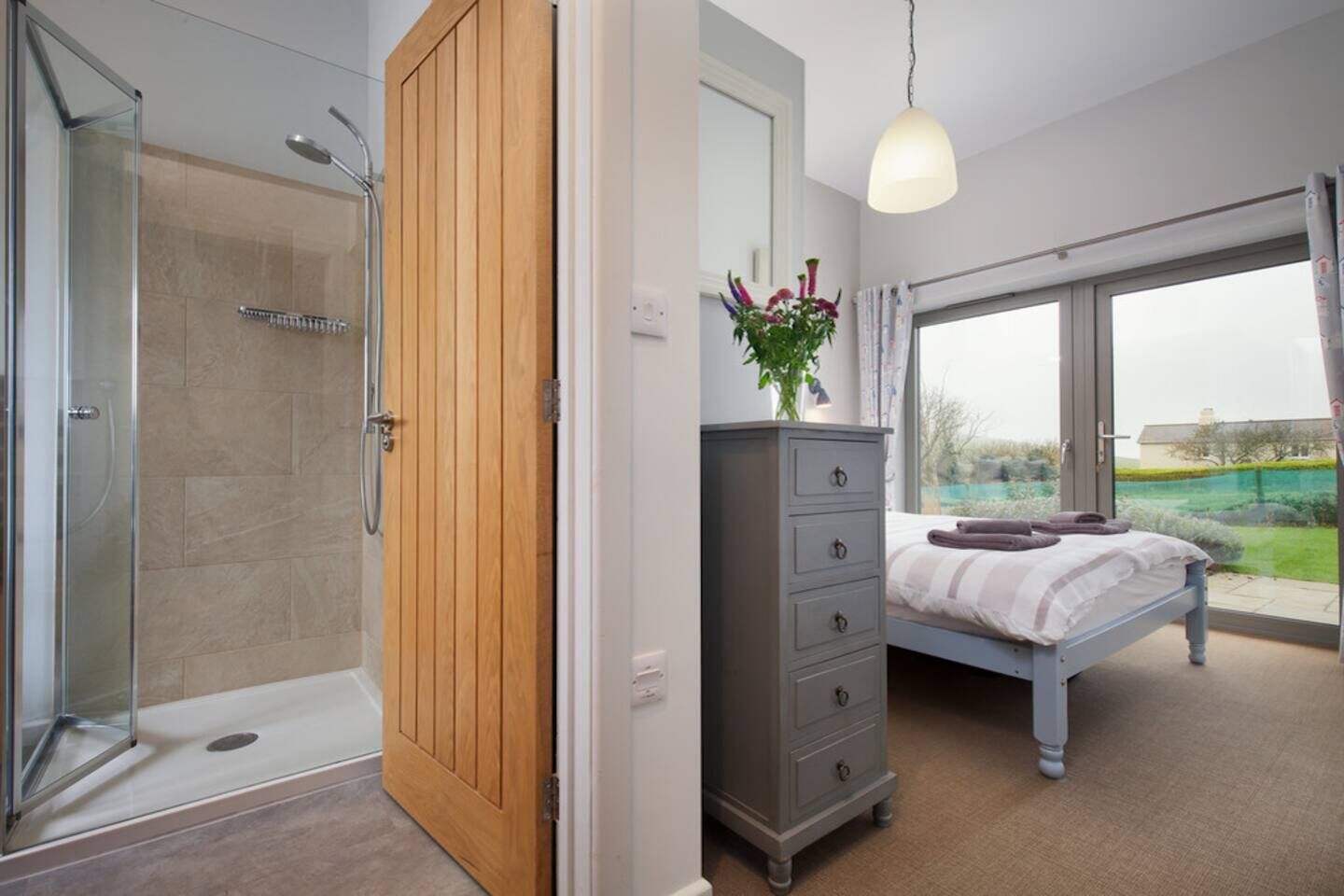 Une chambre à coucher avec un lit, une commode, une douche et une grande fenêtre.