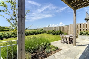 Ein überdachter Patio-Bereich mit Tisch und Stühlen, ein Holzzaun und Blick auf einen angelegten Garten.
