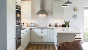 A modern kitchen with white cabinetry, a central island, and a hanging light fixture. - Sloopside - The Annexe, Bantham, South Devon (Bantham)