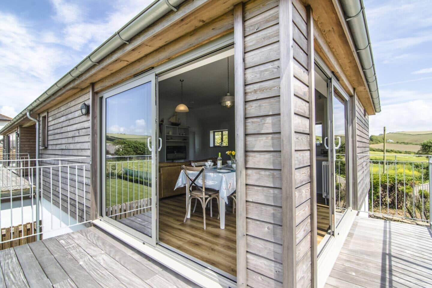 A wooden cabin with a deck, a dining area with a table and chairs, and a large sliding glass door.