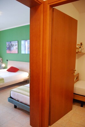 A bedroom with a bed, a wooden door, and a green wall. - Relaxing Flat With Pool in a Quiet Holiday Village (San Michele al Tagliamento)