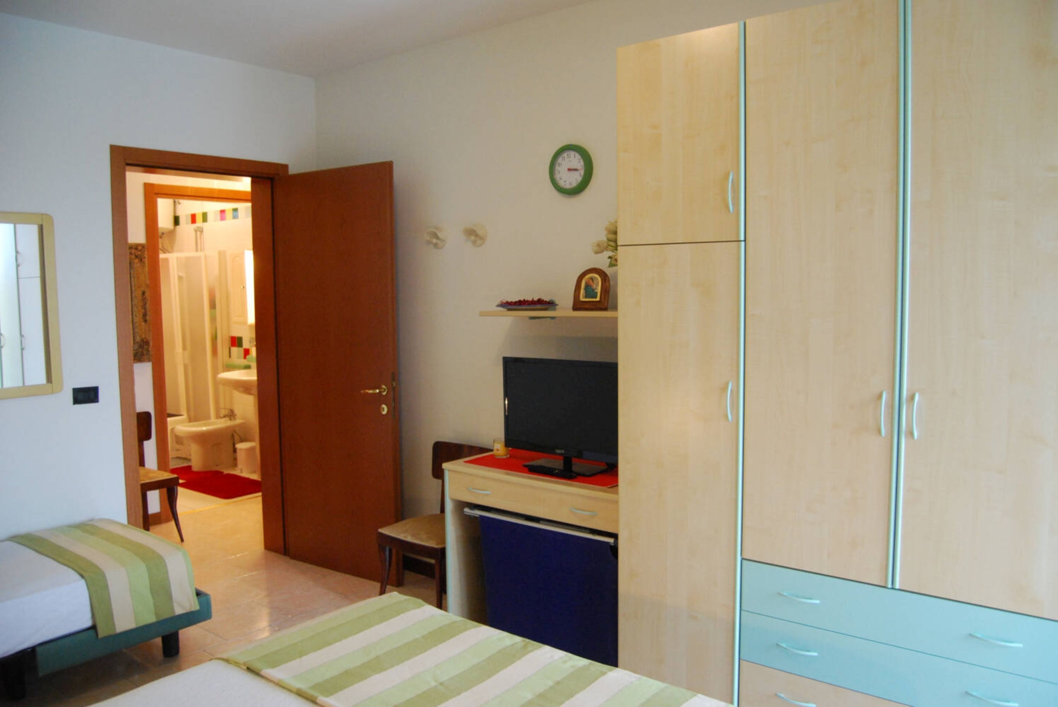A bedroom with a bed, a desk, a wardrobe, and a bathroom visible through an open door.