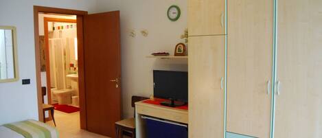 A bedroom with a bed, a desk, a wardrobe, and a bathroom visible through an open door.