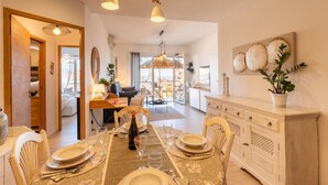 A dining area with a table set for four, a white cabinet with decorative plates, and a view into the living area. - GuestHost - Modern Flat with Lovely Terrace (Sanremo)
