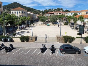 A parking lot with several parked scooters and cars, surrounded by buildings and trees. - Apt in the heart of the village near the sea (Carqueiranne)