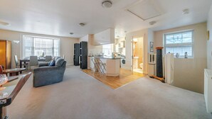 A spacious living area with a sofa, a dining table, and a kitchen area with a counter and appliances. - Retro Art Deco 2Bed with Parking in Thames Ditton - Pass the Keys (Surrey)