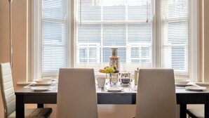 A dining area with a table set for two, a vase with flowers, and a window with blinds. - Retro Art Deco 2Bed with Parking in Thames Ditton - Pass the Keys (Surrey)