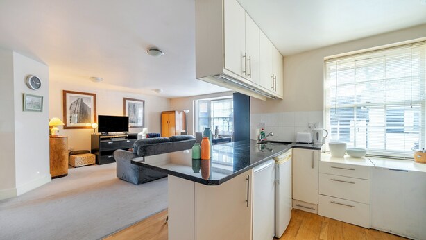 A modern kitchen with white cabinets, a black countertop, and a window with blinds. - Retro Art Deco 2Bed with Parking in Thames Ditton - Pass the Keys (Surrey)