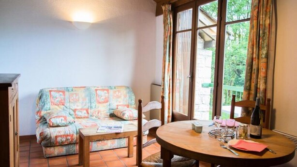 A cozy living room with a sofa, a dining table with chairs, and a window with curtains. - Cottage for 4 People (La Canourgue)
