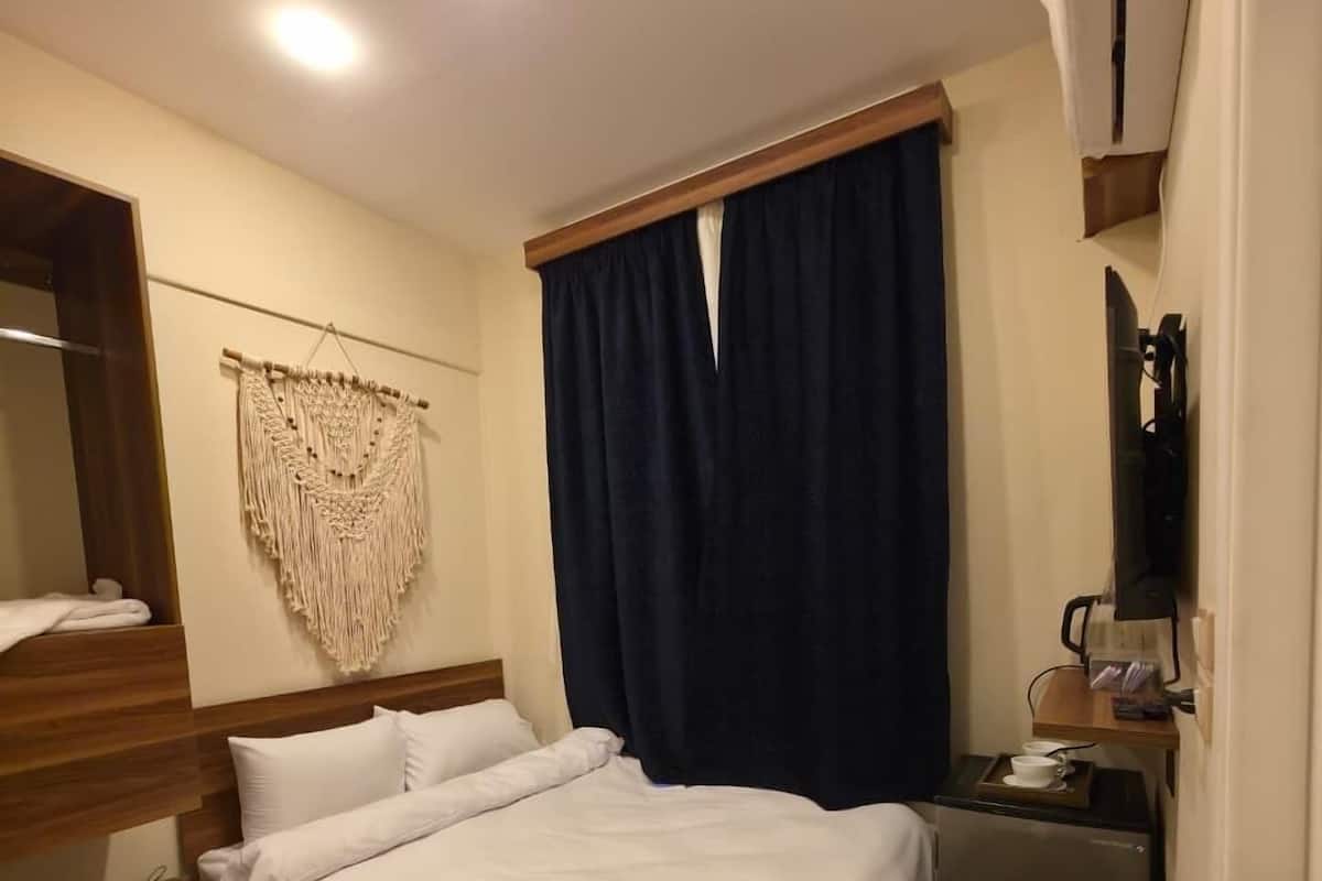 A neatly arranged bedroom with a bed, bedside table, and a small desk with a cup and tissues.