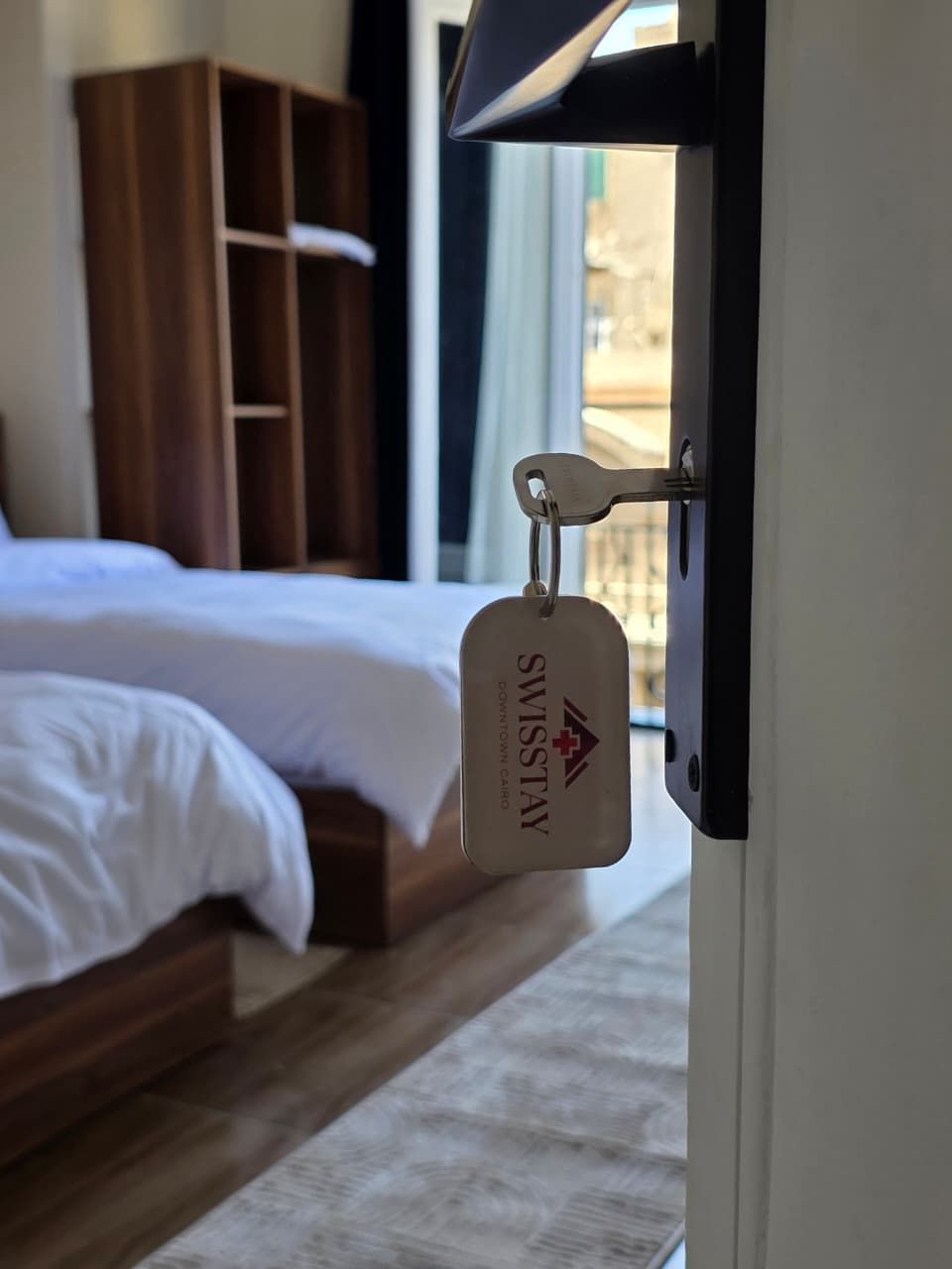 A hotel room with a bed, wooden wardrobe, and a keychain with the hotel's name.