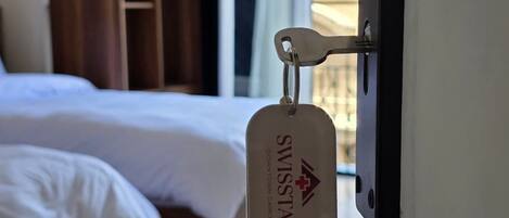 A hotel room with a bed, wooden wardrobe, and a keychain with the hotel's name.