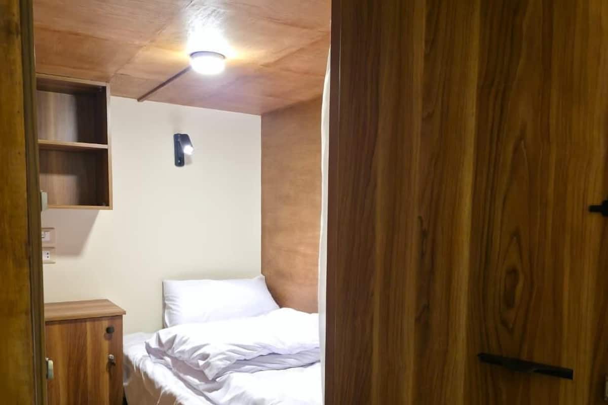 A small, compact bedroom with a single bed, a wooden wardrobe, and a small shelf unit.