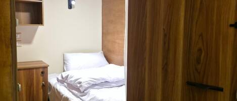 Ein kleines, gemütliches Schlafzimmer mit einem Einzelbett, einem Holzschrank und einer kleinen Regalwand.