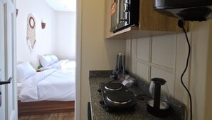 Une cuisine compacte équipée d’un four à micro-ondes, d’une bouilloire et d’une machine à café sur le plan de travail. On aperçoit un lit dans la pièce adjacente.