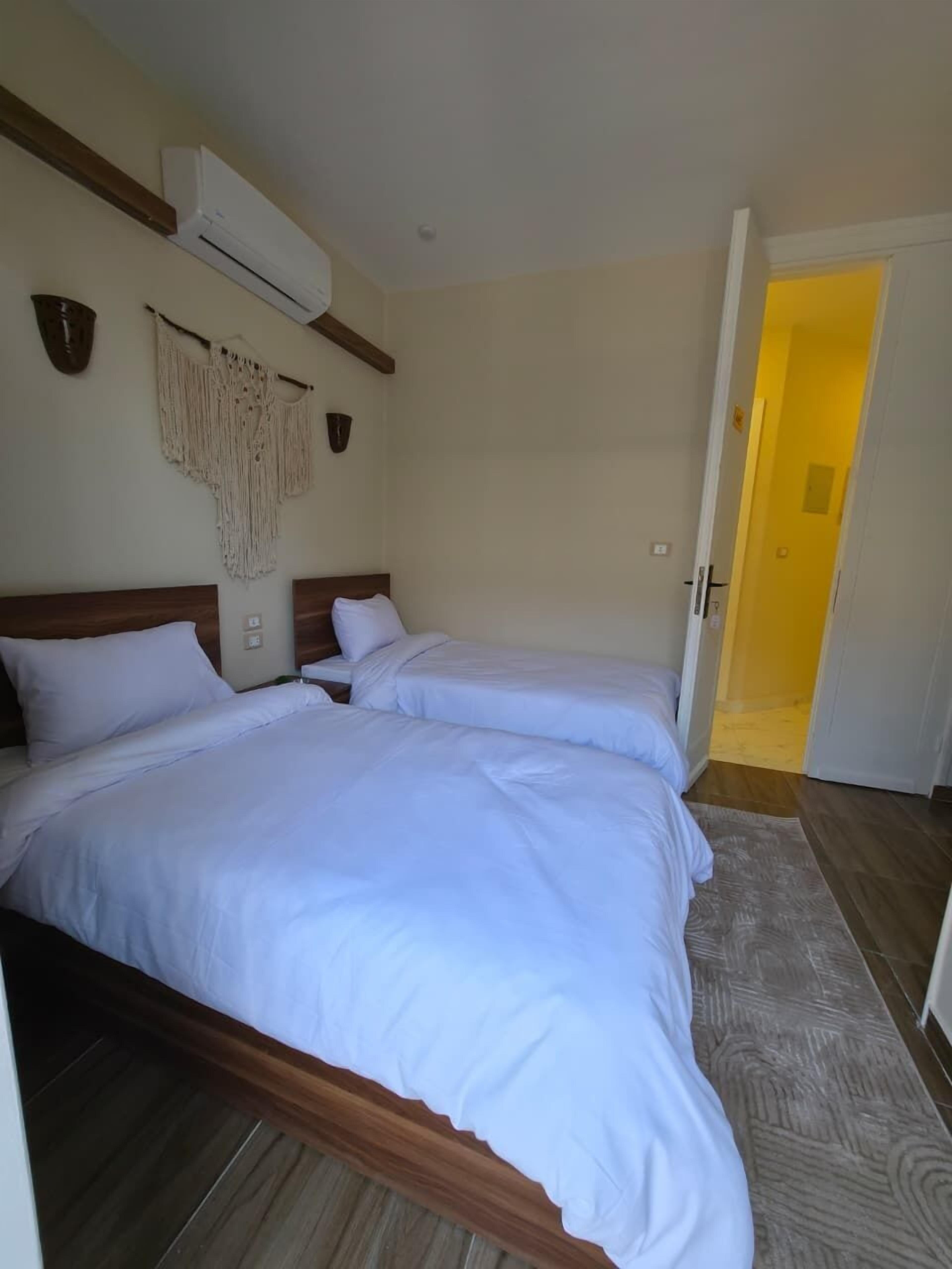 A room with two beds, wooden headboards, a macrame wall hanging, and an air conditioning unit.